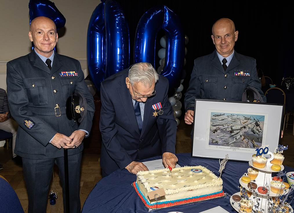 Denis 'cuts the cake', while representatives from RAF Brize Norton stand either side of him.
